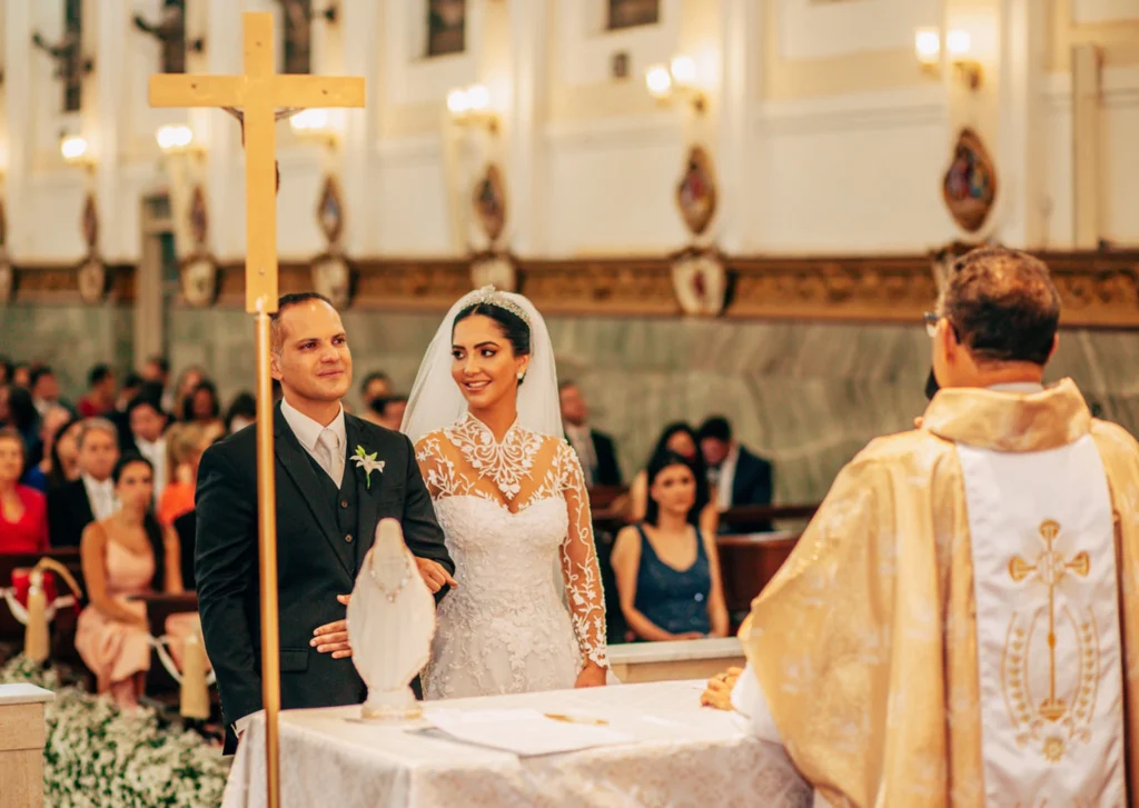 Noivos posando ao lado dos pais sob um altar decorado com flores durante o casamento

