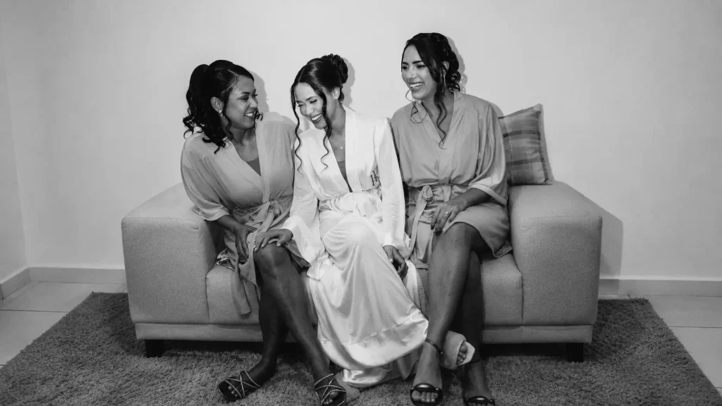Noiva sorrindo ao lado de duas amigas durante os preparativos do casamento
